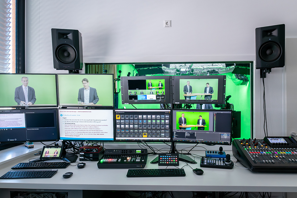 Ein leerer Greenscreen-Raum mit einem modernen, geschwungenen Moderationstisch in der Mitte. Im Vordergrund stehen mehrere Kameras, im Hintergrund ist professionelle Beleuchtung an der Decke montiert.